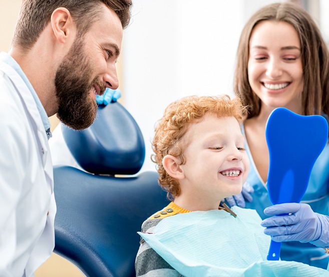 Child smiling at reflection with dentist and assistant