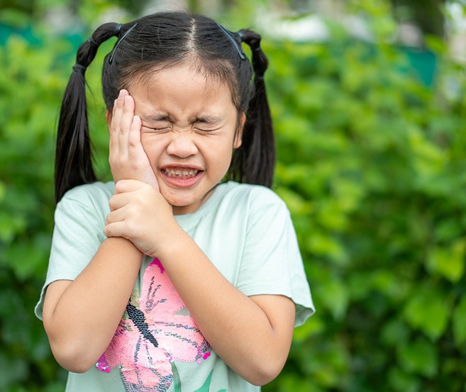 Little girl outside holding hand to face squinting in pain