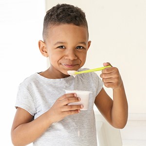 Little boy eating yogurt with yellow spoon